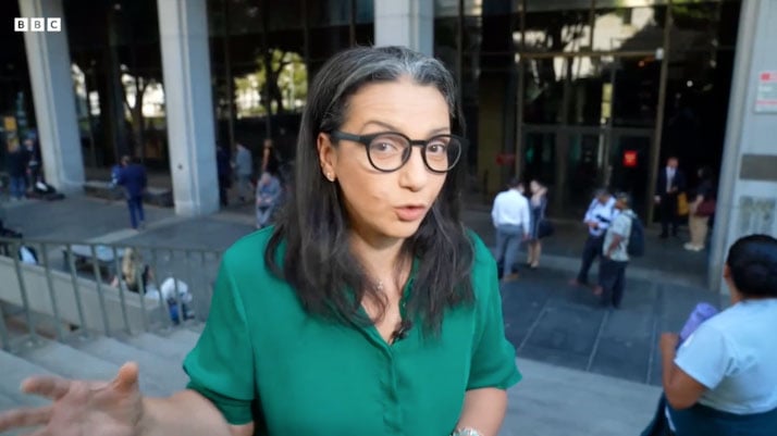 A BBC news commentator presenting outside of a courthouse